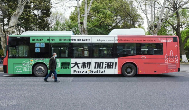 A man wearing a face mask in Hangzhou, China walks past a bus with a message supporting Italy in its efforts against the COVID-19 coronavirus