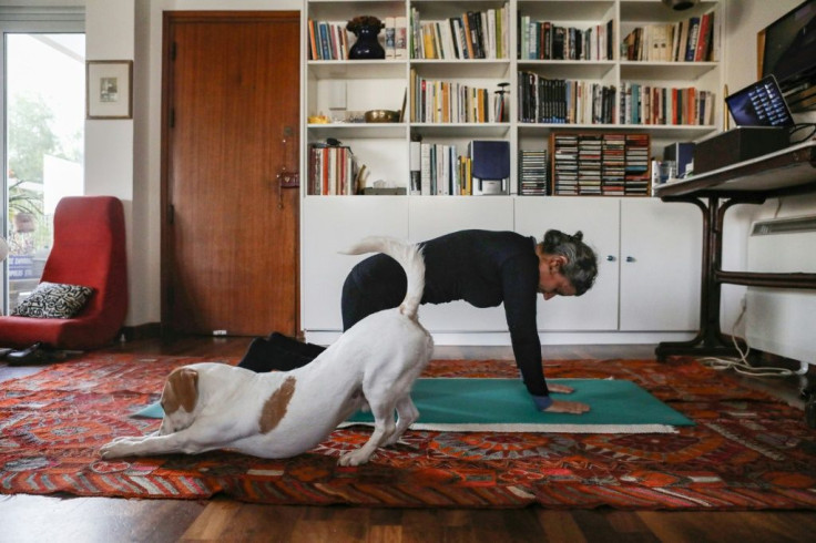 A woman follows an online pilates class at home, as her dog Elvis stretches next to her