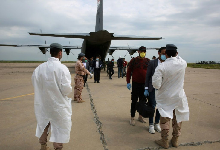 Members of the Iraqi military check the temperatures of people wearing masks to protect against the coronavirus at the Qayyarah air base