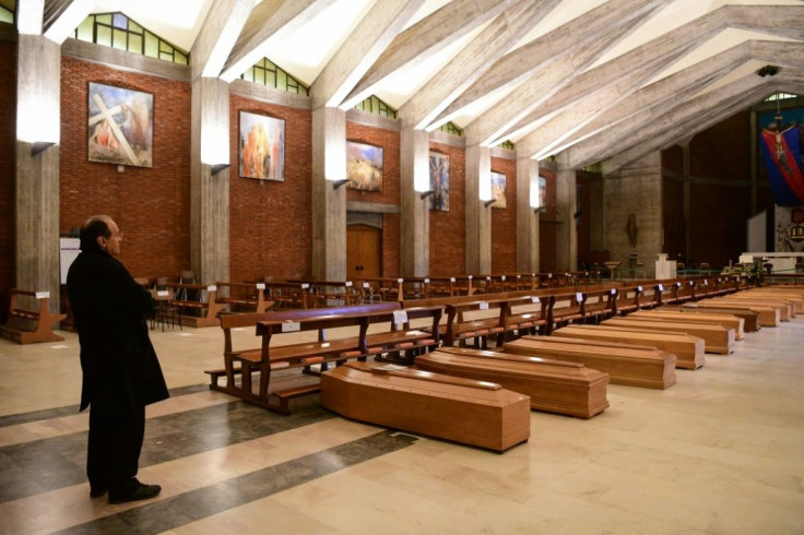 A priest stands by coffins stored in  the church of San Giuseppe near Bergamo, Italy