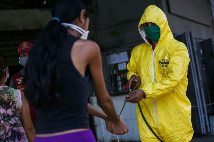 A worker wearing a protective suit disinfects a customer's hands at a municipal market in Caracas