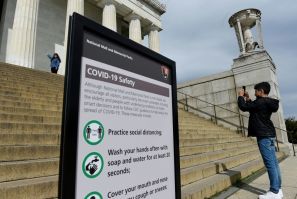 Tourists take pictures near a sign informing about coronavirus safety measures at the Lincoln Memorial on March 27, 2020 in Washington, DC