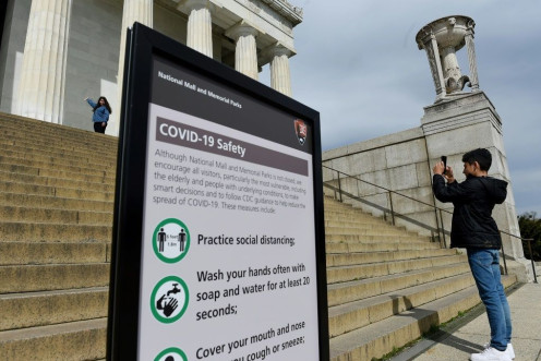 Tourists take pictures near a sign informing about coronavirus safety measures at the Lincoln Memorial on March 27, 2020 in Washington, DC