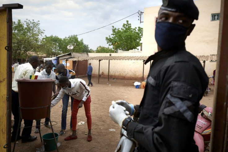 Voters wash their hands before casting their ballots as a member of the security forces looks on