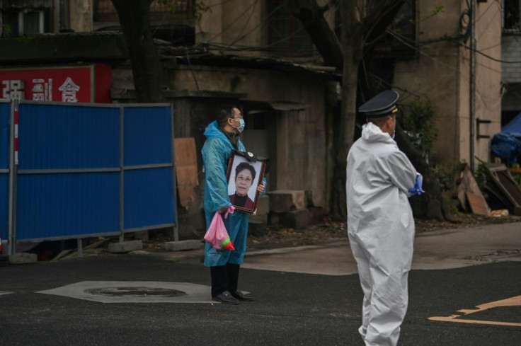 As small groups gathered quietly around gravesites on the hillside in Wuhan, a man draped in a blue plastic protective poncho stood silently near the cemetery entrance, holding a photo portrait of a woman who had died