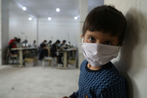 A child looks on as volunteers gather in a sewing workshop to make protective face-masks in the northeastern Syrian city of Idlib