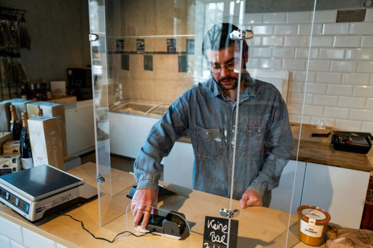 A cashier works from behind a plexiglass screen at a grocery store in Berlin