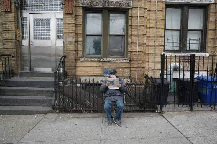 A man wearing a surgical mask reads the newspaper on the sidewalk in Brooklyn, New York, amid a surge in news readership during the coronavirus pandemic