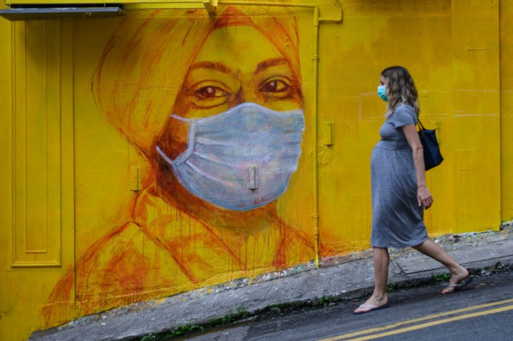 A pregnant woman wearing a face mask as a precautionary measure walks past a street mural in Hong Kong