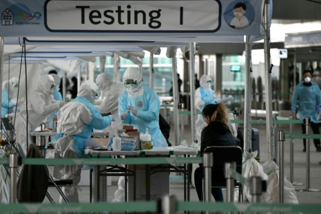 Medical staff wearing protective clothing take test samples for the COVID-19 coronavirus from a foreign passenger at a virus testing booth outside Incheon international airport near Seoul