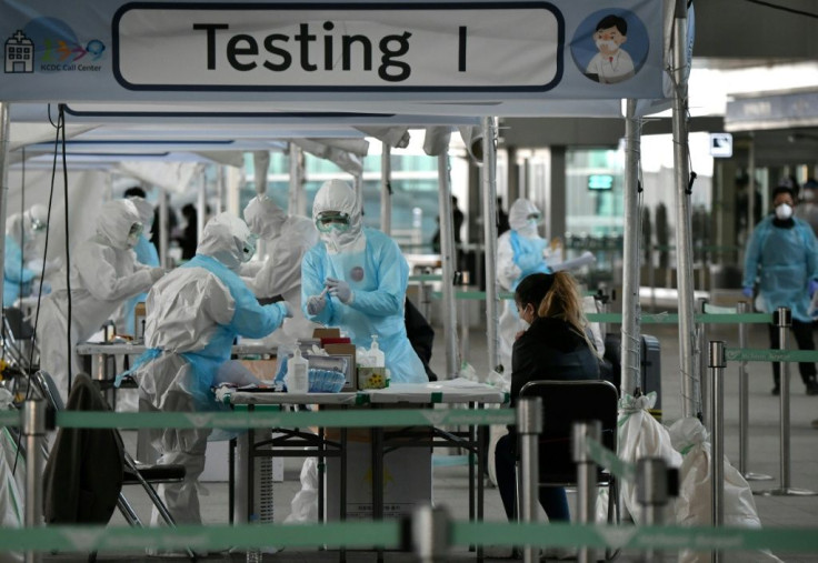 Medical staff wearing protective clothing take test samples for the COVID-19 coronavirus from a foreign passenger at a virus testing booth outside Incheon international airport near Seoul