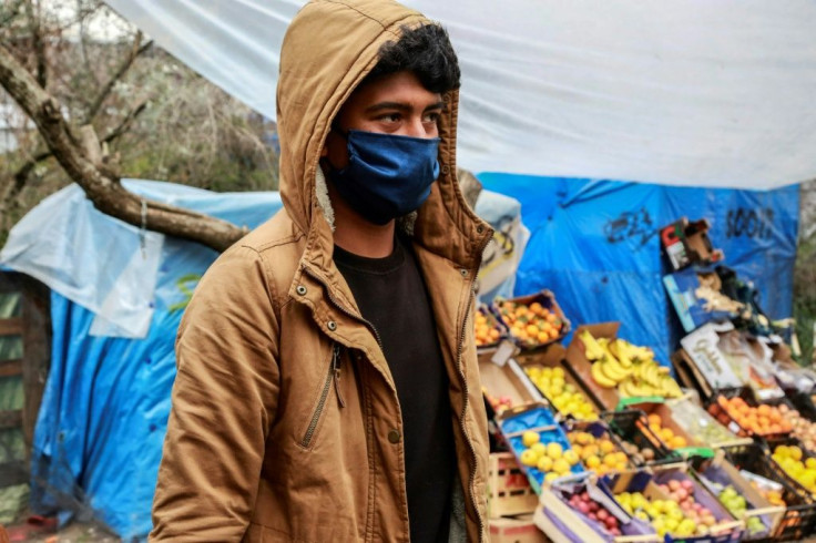 A migrant wearing a facemask walks by a fruit and vegetable stall at the Moria camp