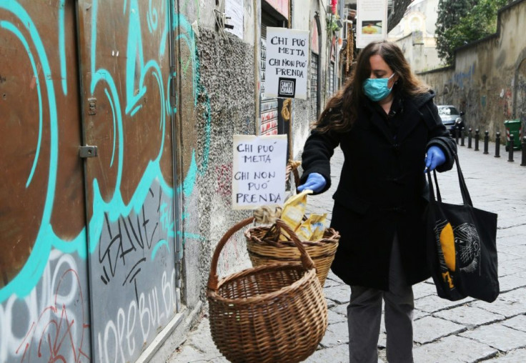 A woman puts food in a solidarity basket displayed with a note reading, "Who can put, who cannot take" in Naples, as Italy sees evidence it may have made it through the worst of the coronavirus pandemic