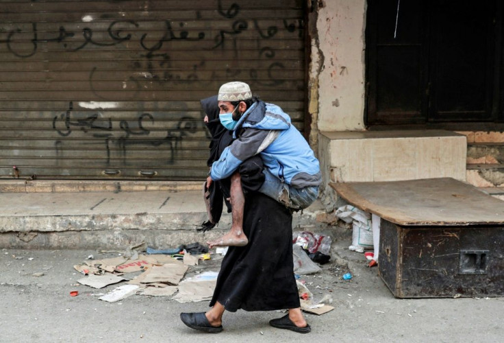 A woman carries a disabled man wearing a protective face mask in the Sabra refugee camp in Lebanon where vulnerable Syrian and Palestinian refugees are bracing for the coronavirus