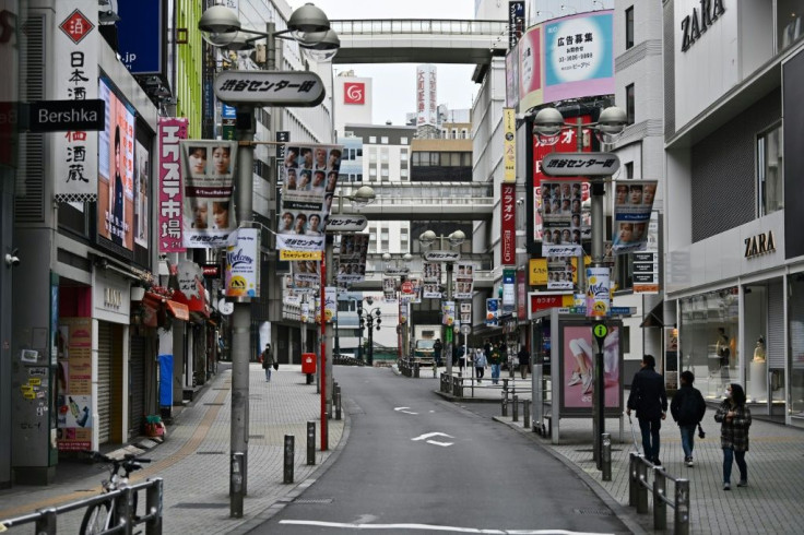 A handful of pedestrians walk down a quiet street in the usually busy shopping area in Shibuya in Tokyo