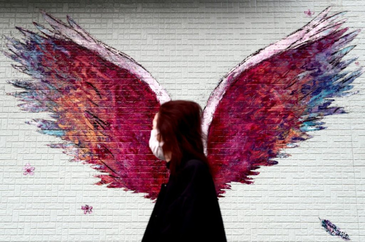 A woman wearing a face mask amid concerns over COVID-19 walks past a graffiti of wings in Tokyo