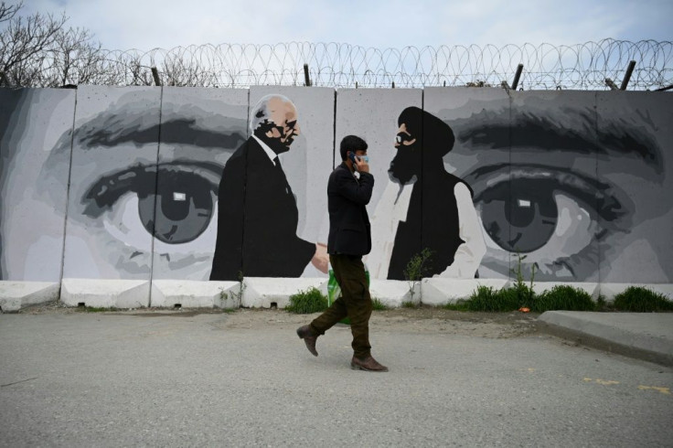 A man wearing a facemask against coronavirus walks past a wall painted with images of US Special Representative for Afghanistan Reconciliation Zalmay Khalilzad and Taliban co-founder Mullah Abdul Ghani Baradar, in Kabul