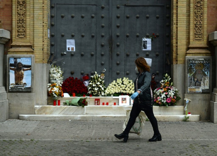 A woman walks past a church in Seville, adorned with flowers and candles left by the faithful after Easter processions were cancelled