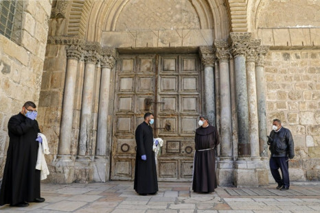Priests wearing face masks and gloves stand in front of the closed door of the Holy Sepulchre Church in Jerusalem's Old City earlier this month