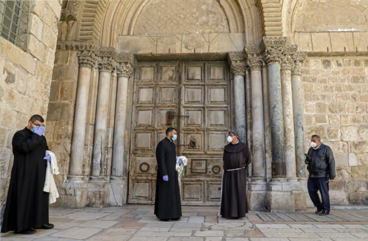 Priests wearing face masks and gloves stand in front of the closed door of the Holy Sepulchre Church in Jerusalem's Old City earlier this month