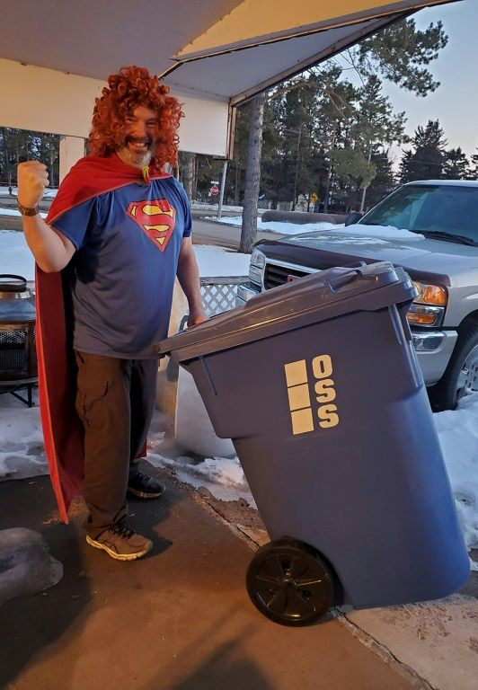 Christine Leland shared a photo of her husband wheeling a bin through the Canadian snow in a superman T-shirt, wig and red towel for a cape