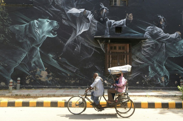 A rickshaw driver carries passengers wearing facemasks past a mural in the Lodhi Art District in New Delhi