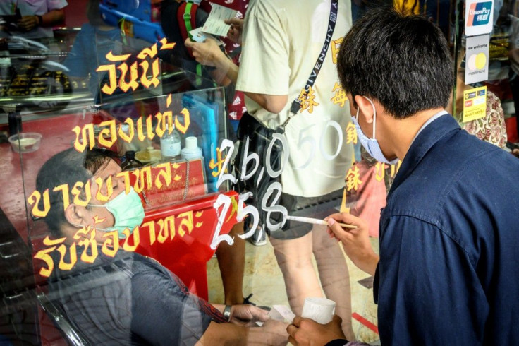 An employee paints the latest price of gold on a shop window in the Thai capital