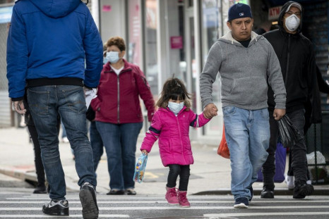 A girl wearing a mask  walks down a street in the Corona neighborhood of Queens