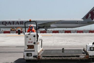 A masked worker drives a loader in front of a Qatar Airways jet at Doha's Hamad International airport