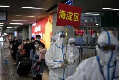 Transport personnel wearing hazmat suits guide travellers arriving from Wuhan to buses, which will take them to their quarantine locations, at Beijing West Railway Station