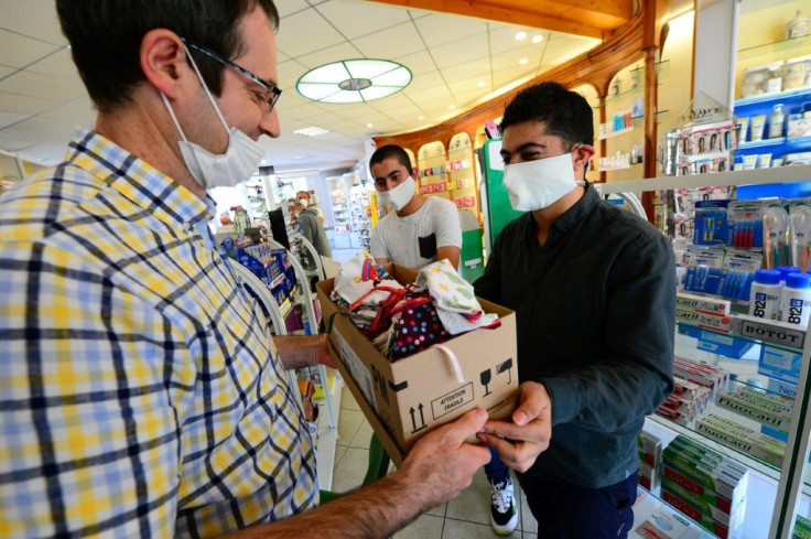 Syrian refugee Mustapha Shikho hands over a box of protective masks to the local pharmacist