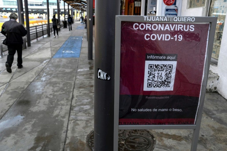 Commuters walk past a sign warning about the COVID-19 at San Ysidro port of entry, in Tijuana, Baja California state, Mexico