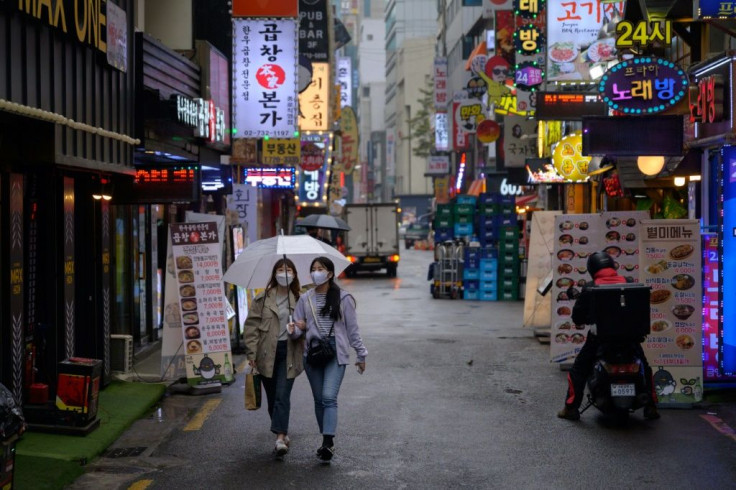 Two women in facemasks walk beneath an umbrella in a Seoul alleyway