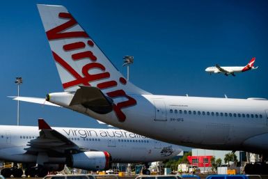 Virgin Australia aircraft are parked on the tarmac at Brisbane International airport while a plane from Qantas, the only other Australian full-service carrier, flies in the background