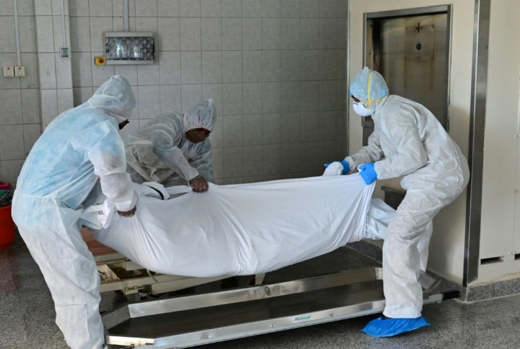 Employees lift the body of a COVID-19 victim before loading it into the furnace at the New Sonapur Hindu crematorium in Dubai