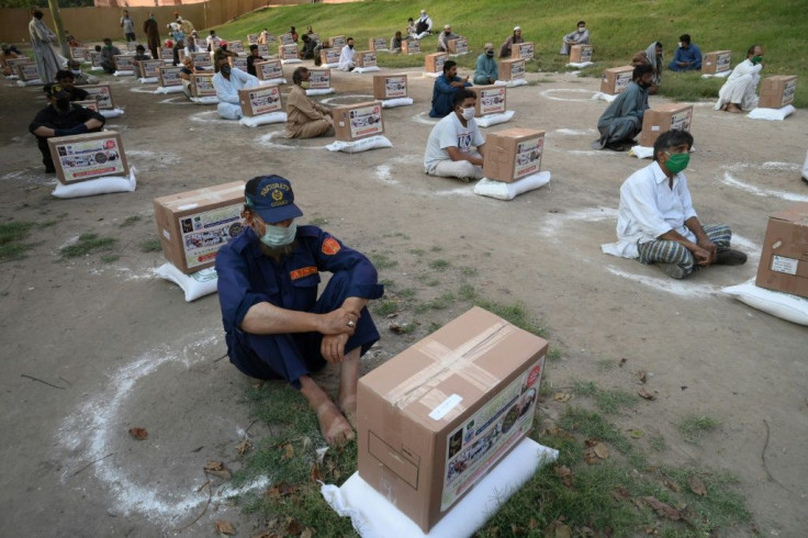 People in need sit maintaining social distancing after collecting free food items outside the Badshahi mosque in Lahore, Pakistan