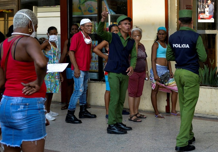 Police stand guard to ensure a minimum of distance between shoppers lined up in Havana
