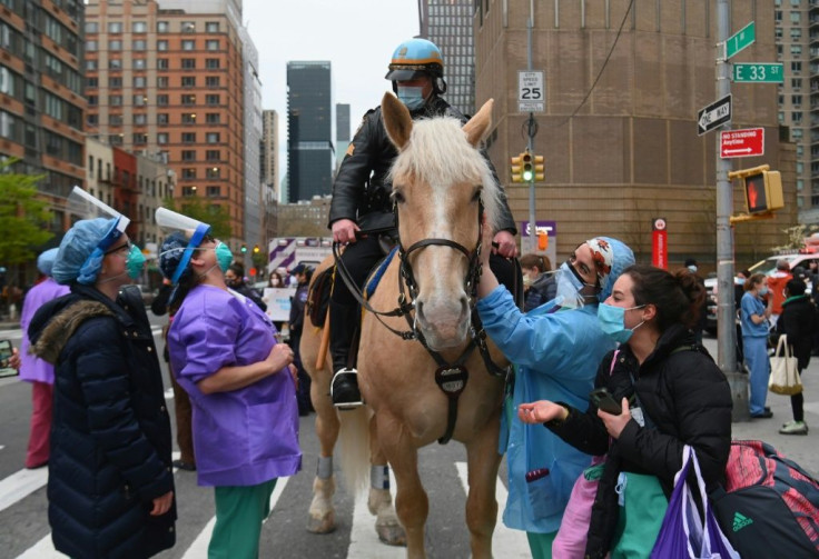 Healthcare workers pet a NYPD horse as people cheer and applaud to show their gratitude to essential workers outside NYU Langone Health hospital in New York City