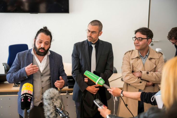 Attorney Patrick Kroker (C) and co-plaintiffs Wassim Mukdad (L) and Hussein Ghrer answer journalists' questions outside the courtroom during a break in a trial against two Syrian defendants accused of state-sponsored torture in Syria