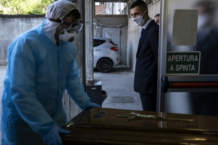 A worker at Palmero funeral home watches a colleague in protective gear as he moves a coffin containing a coronavirus victim at the morgue in Saluzzo hospital in northwestern Italy