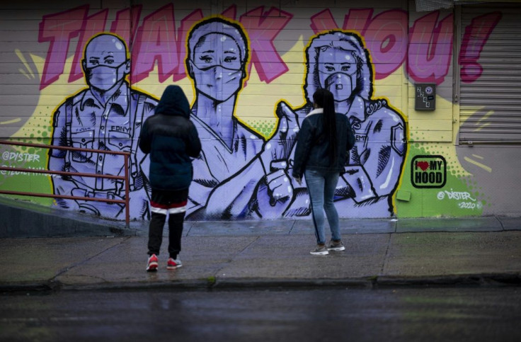 Two woman stand in front of a mural by artist @Dister picturing first responders with masks on and a Thank You message during the novel coronavirus pandemic in the Harlem neighbourhood of Manhattan in New York City