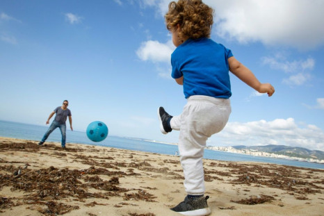 A child plays footbal with his father at Can Pere Antoni Beach in Palma de Mallorca, Spain