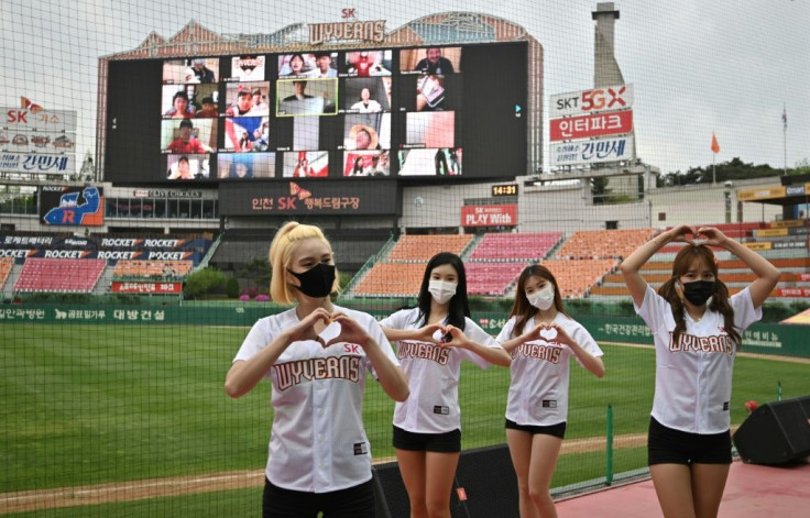 Cheerleaders pose in front of a big screen displaying baseball fans cheering from their homes during the opening game of South Korea's new baseball season