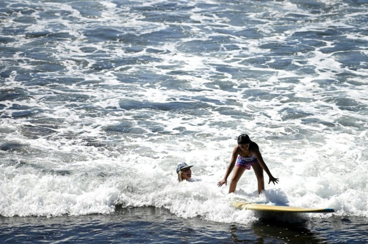 Surf's up at El Zonte beach in El Salvador, where a girl stands on a surf board next to her volunteer instructor