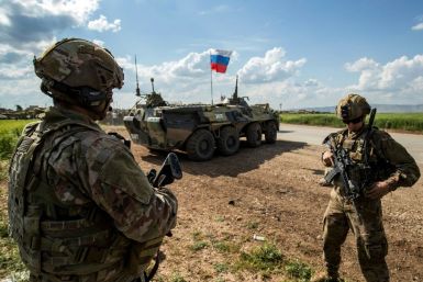 US soldiers stand along the side of a road across near a Russian military armoured personnel carrier (APC), near the village of Tannuriyah in the countryside east of Qamishli in Syria's northeastern Hasakah province on May 2, 2020