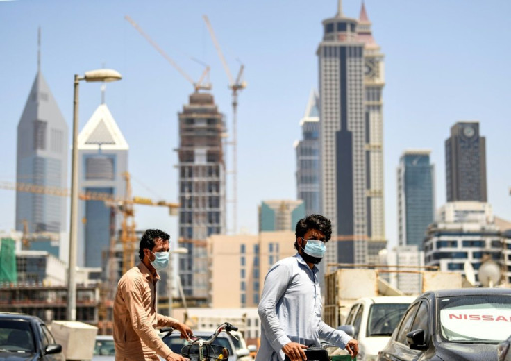 Foreign workers clad in masks to protect against coronavirus push bicycles along a street in the Satwa district of Dubai