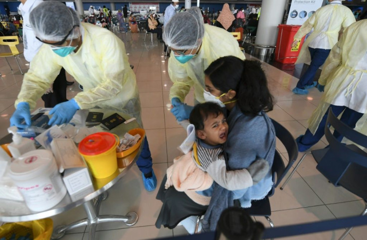 Health workers take a blood test from a child carried by an Indian woman at the Dubai International Airport before they leave the Gulf Emirate on a flight back to their country on May 7, 2020