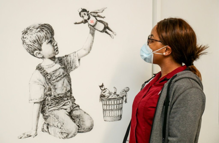 A University Hospital Southampton staff member looks at an artwork by street artist Banksy called "Game Changer", showing a boy playing with a nurse superhero toy with figures of Batman and Spiderman discarded in a basket