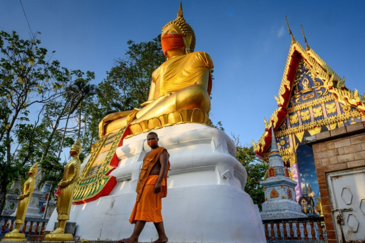 A monk walks in front of a giant Buddha statue wearing a face mask at Wat Nithet Rat Pradit temple in Pathum Thani outside Bangkok