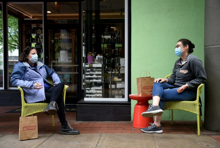 Friends wearing face masks chat in front of a shop during the outbreak of COVID-19  in Arlington, Virginia